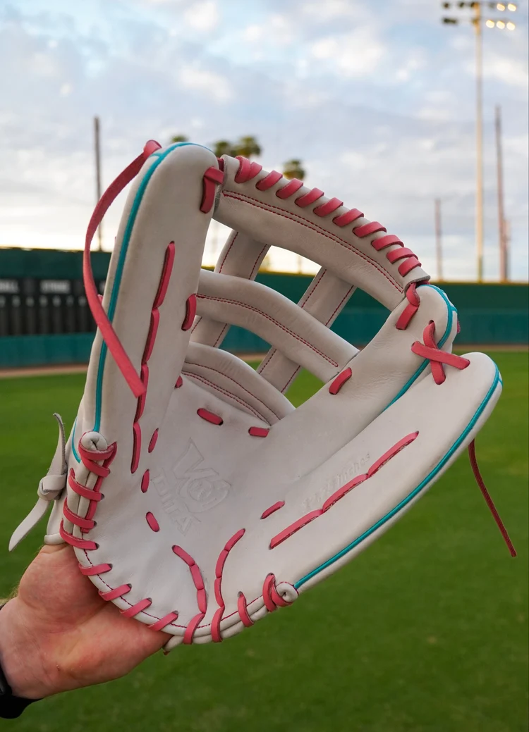 A custom Wodita LOCK3 glove held up on the field, off-white leather with pink laces and turquoise trim